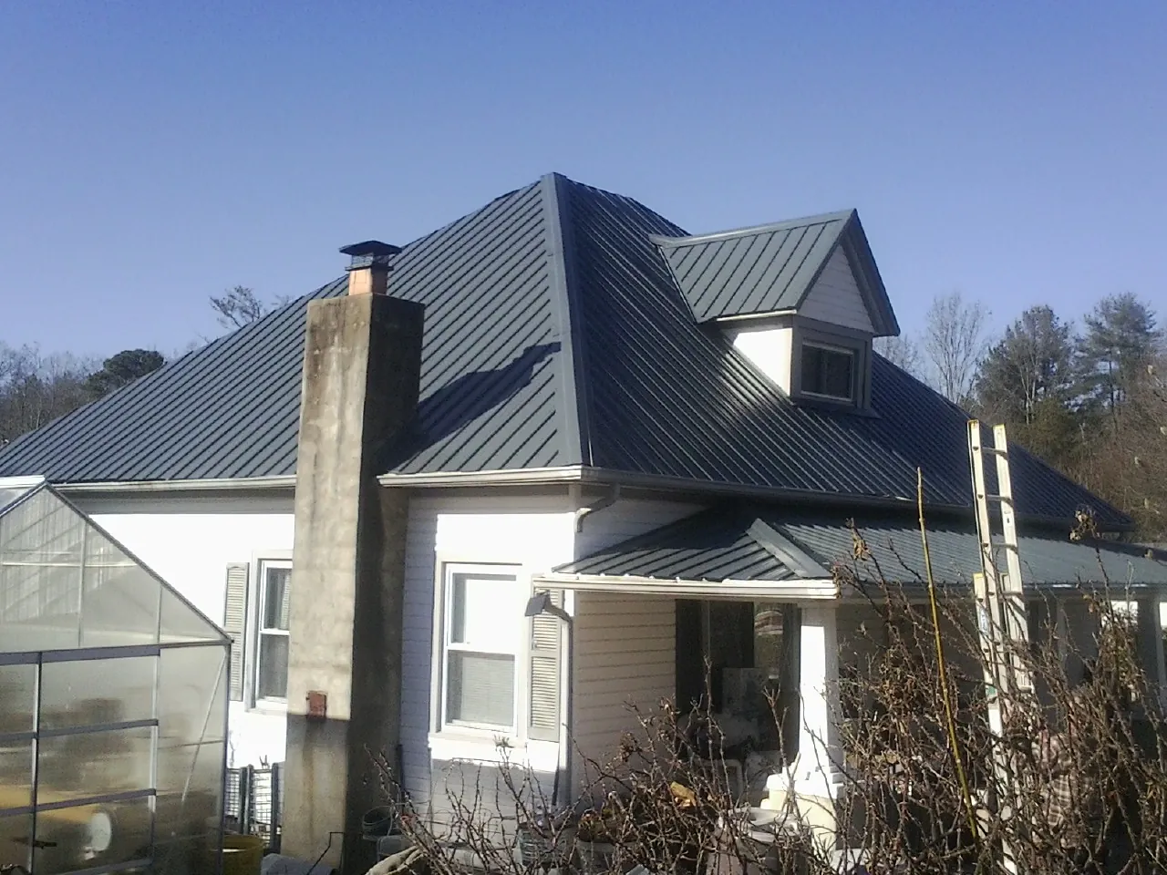 Dark blue standing seam metal roof on a white farmhouse with dormer — Slate & Tile Roof Repair by Roofing Brothers in Lapine