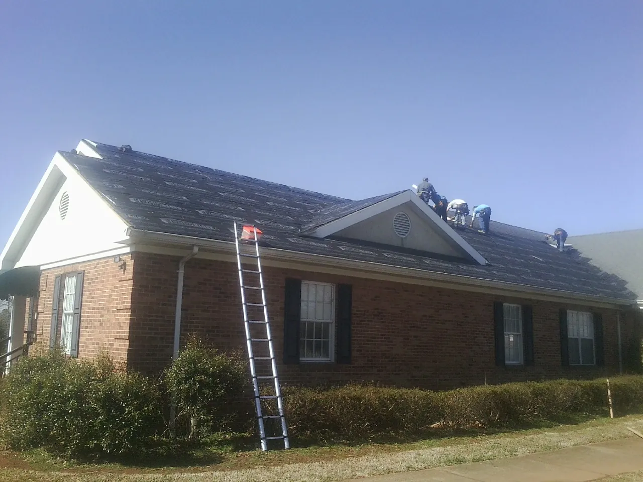 Crew tearing shingles off a brick ranch roof with a ladder set — Emergency Roof Repair work by our crew in Lapine