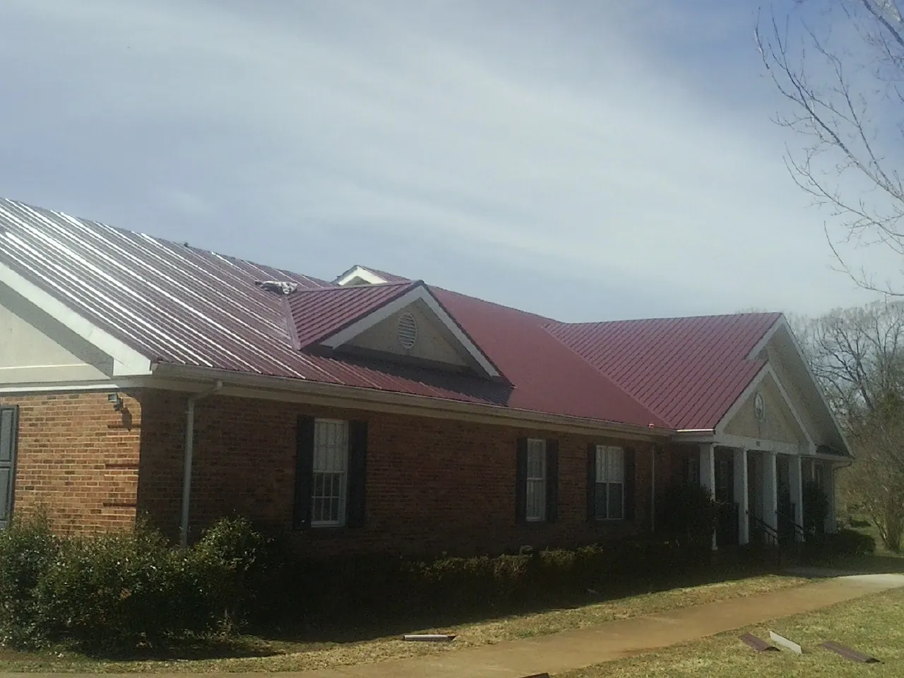 Red metal roof with gabled entries on a long brick building, from a Hail Damage Roof Repair job in Lapine