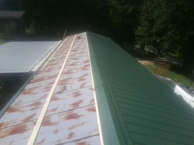 Old rusted panels beside newly installed green metal roofing — Wind Damage Roof Repair by Roofing Brothers in Lapine