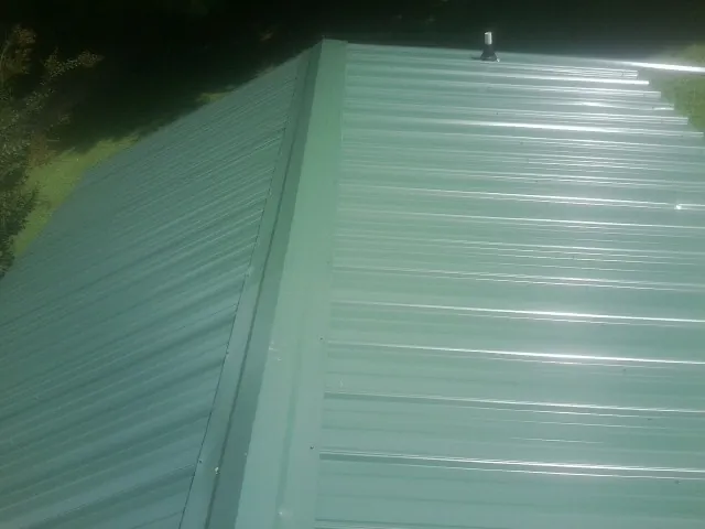 New green metal panels meeting at the ridge of a roof — Flat Roof Repair work by our crew in Lapine
