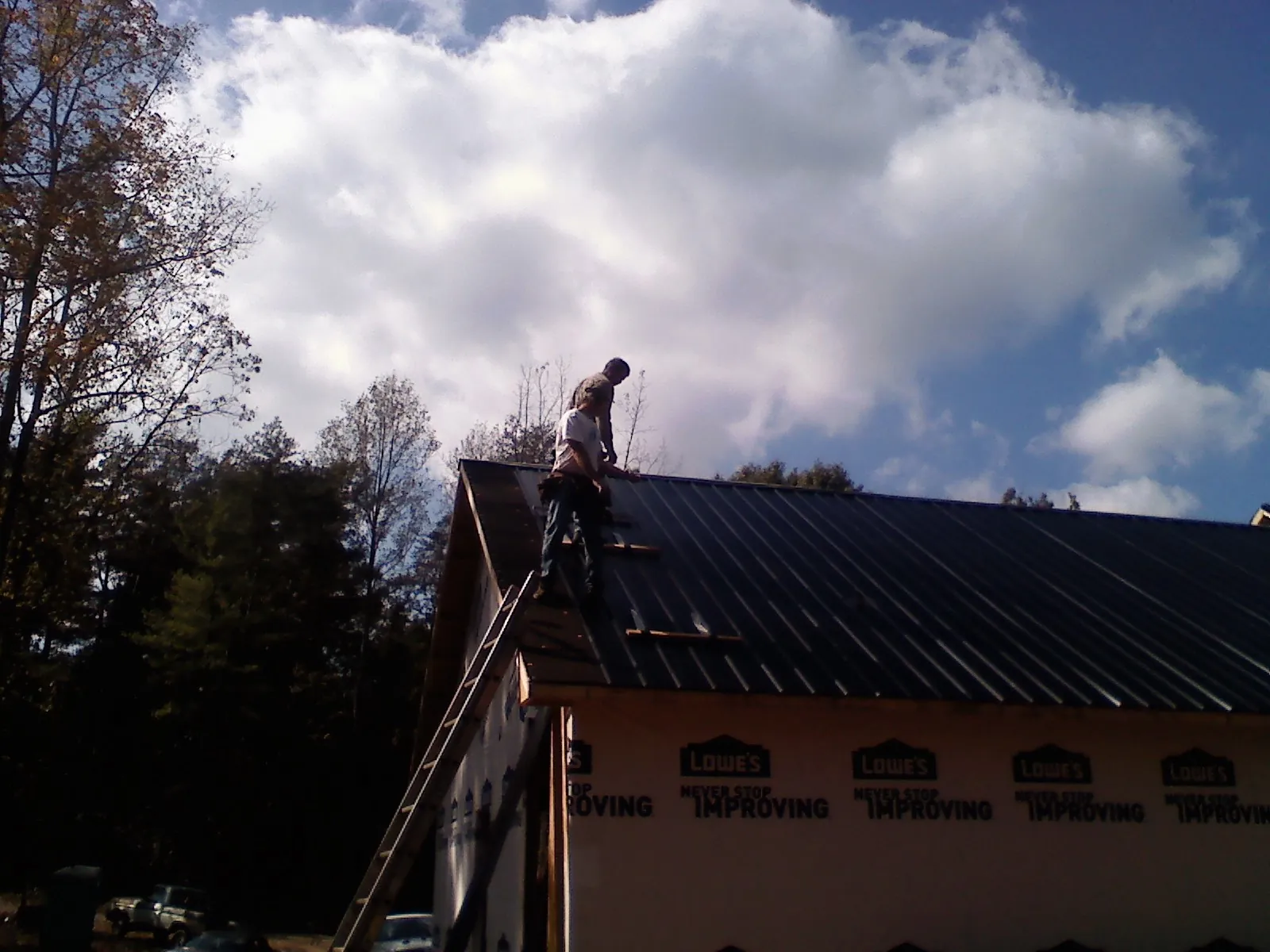 Roofer fastening dark metal panels high against a cloudy sky, from a Roof Inspection job in Lapine