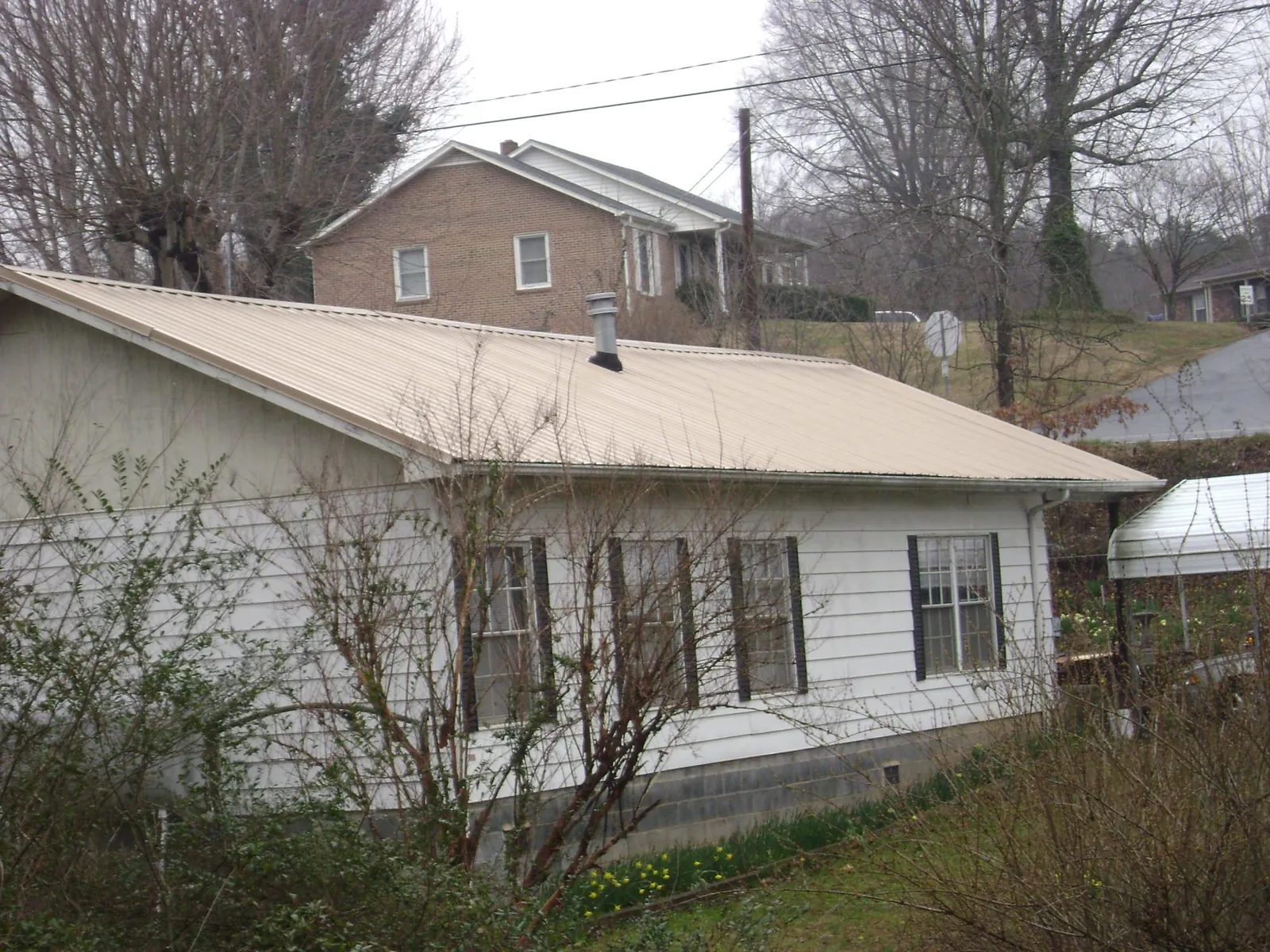 Tan metal roof on a white sided house set into a hillside — Commercial Roofing by Roofing Brothers in Lapine