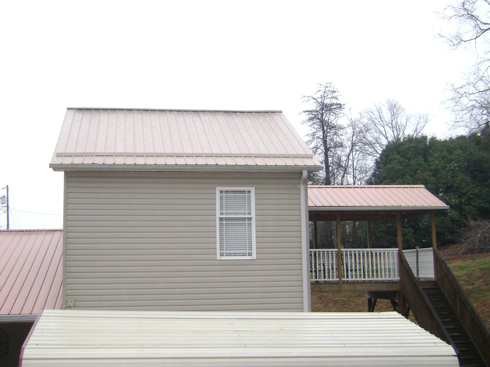 Tan metal roofs on a two story addition and attached porch, from a Roof Replacement job in Lapine